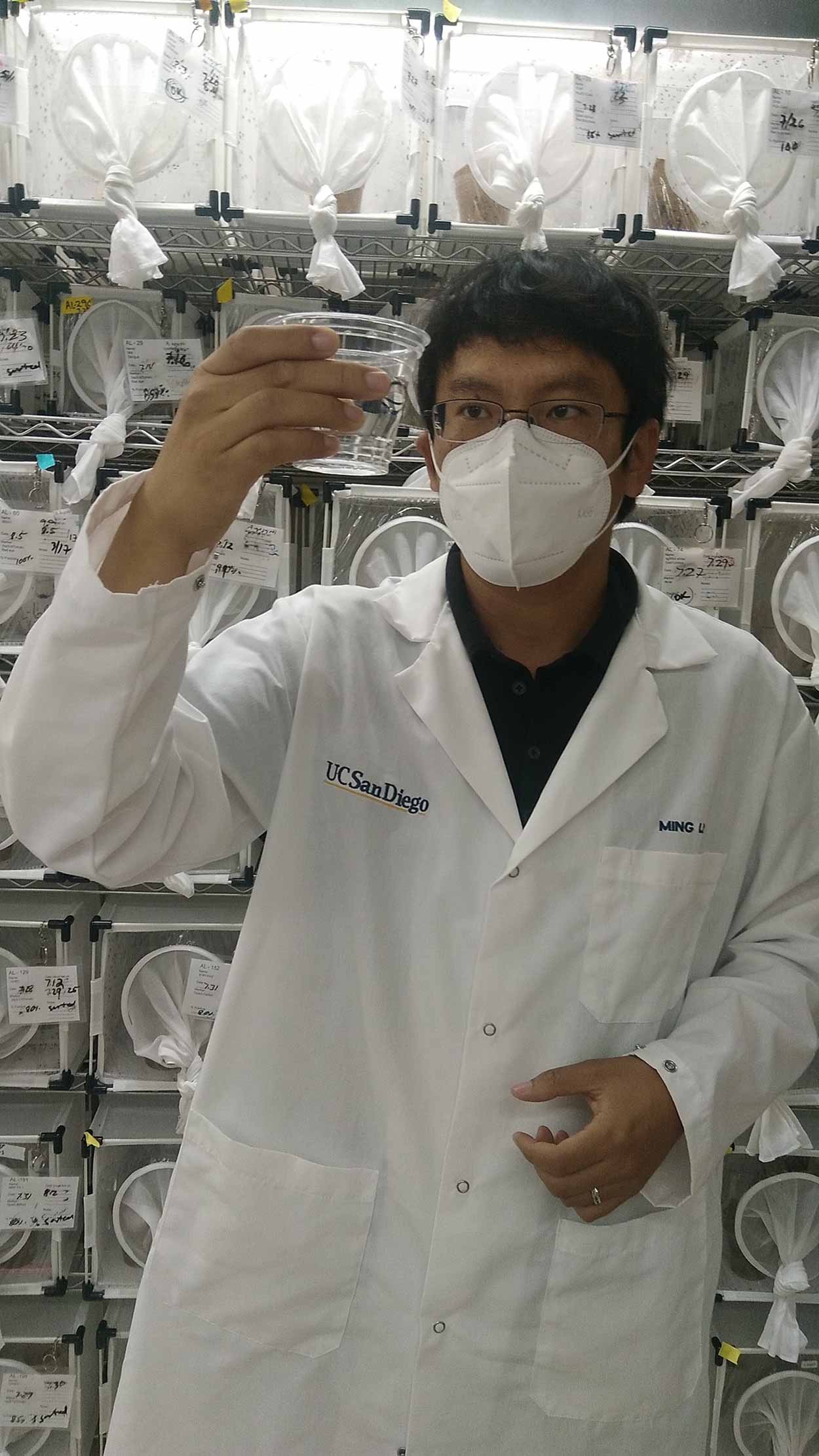 Man in lab coat holding up and observing a cup with a clear liquid