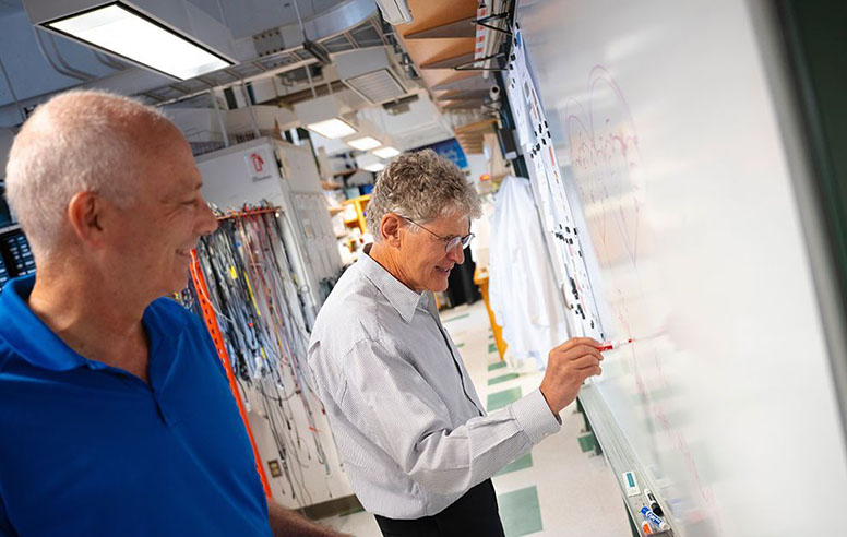 Professor David Kleinfeld works at a white board in his lab.